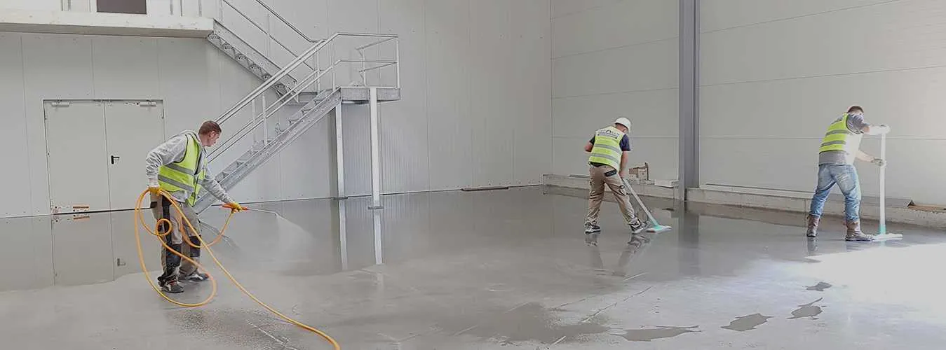 Three construction workers wearing safety vests and helmets are applying a coating