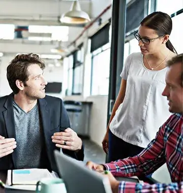 Three diverse employees collaborating around laptop computer in contemporary open office workspace environment